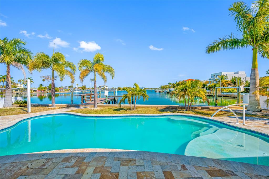 A swimming pool sits on a stone patio overlooking a canal with palm trees — 17161 2ND STREET E, NORTH REDINGTON BEACH, FL