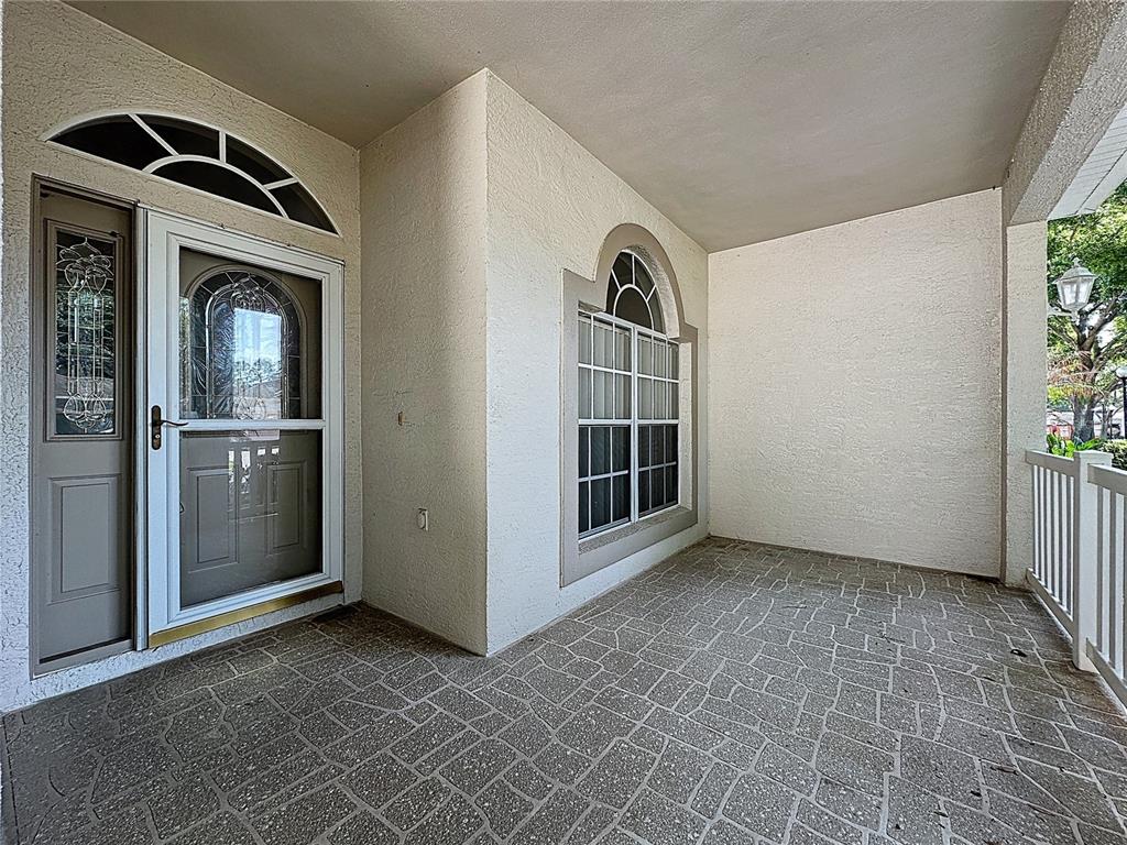 A covered porch features a stone-patterned floor, a front door with a storm door, and windows — 2308 TWICKINGHAM COURT, CLERMONT, FL