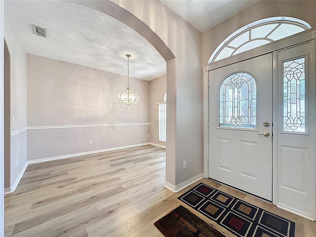 An entryway with a white front door leads into a dining room with wood-look flooring — 2308 TWICKINGHAM COURT, CLERMONT, FL