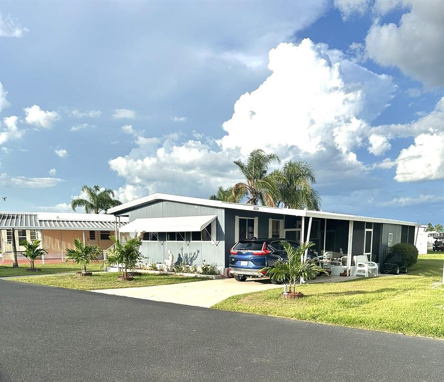 A gray manufactured home with a carport, driveway, and palm trees under a cloudy sky — 315 BEAVER LANE, HAINES CITY, FL