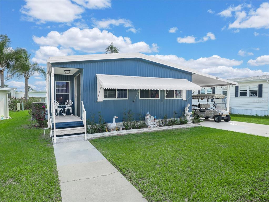 A blue mobile home with a white awning, front porch, and a golf cart parked nearby — 315 BEAVER LANE, HAINES CITY, FL