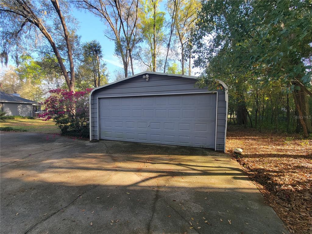 A detached gray metal garage with a single large roll-up door sits on concrete — 8028 SE 129TH PLACE, SUMMERFIELD, FL
