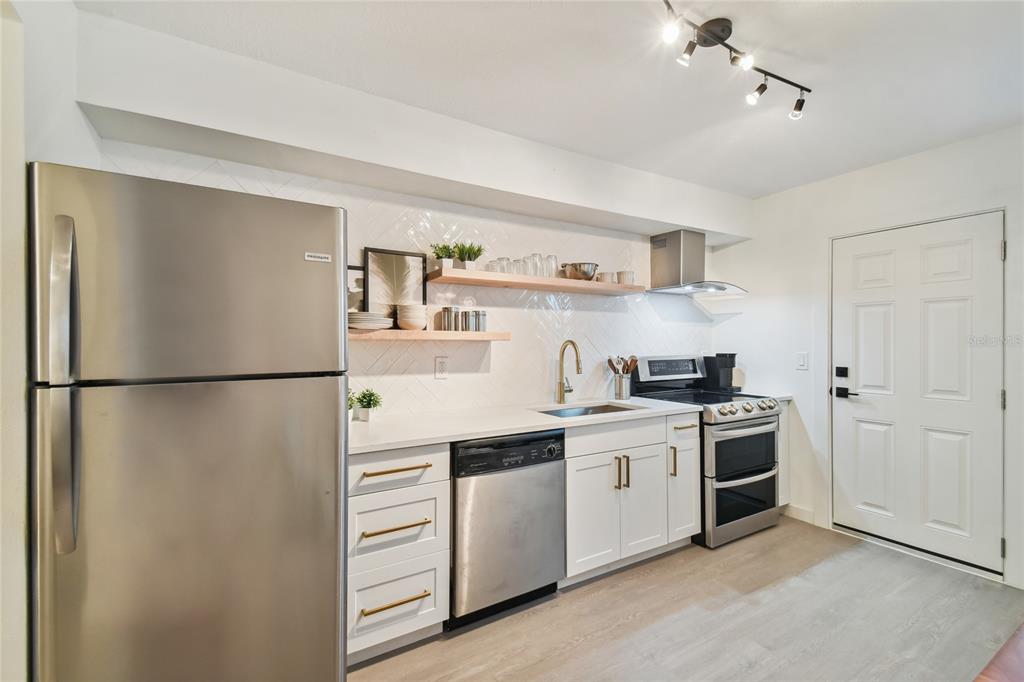 A modern kitchen features white cabinets, stainless steel appliances, open wood shelving, and light flooring — 6422 S ADELIA AVENUE, TAMPA, FL