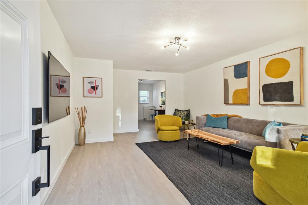 A living room features a gray sofa, yellow armchairs, a black rug, and wall art — 6422 S ADELIA AVENUE, TAMPA, FL