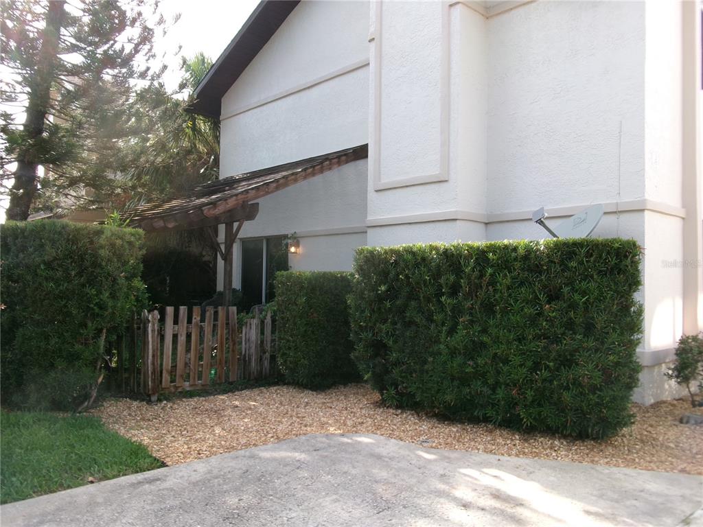 A white stucco building exterior features a small wooden pergola, a fence, and manicured hedges — 1061 ARAGON AVENUE UNIT 1061, WINTER PARK, FL