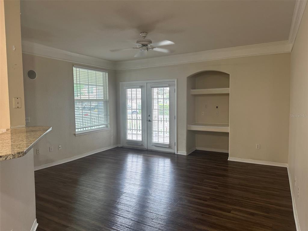 A living room features dark wood-look flooring, a ceiling fan, French doors, and built-in shelving — 3324 PARKCHESTER SQUARE BOULEVARD UNIT 102, ORLANDO, FL