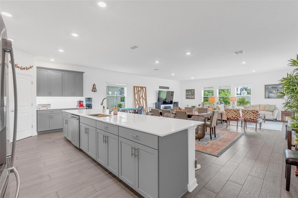 A modern open-concept kitchen features gray cabinetry, a large white island, and wood-look flooring — 11941 LANGUAGE WAY, ORLANDO, FL