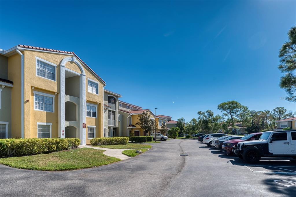 An exterior view of a multi-story yellow apartment building with a parking lot — 5551 BENTGRASS DRIVE UNIT 11-303, SARASOTA, FL
