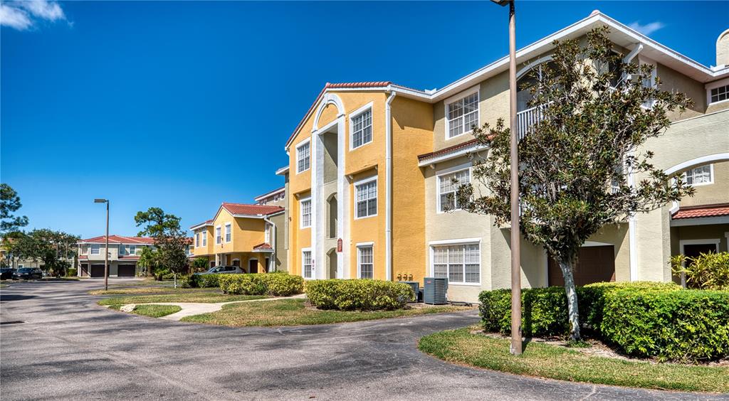 A multi-story apartment building with yellow and beige stucco walls under a clear blue sky — 5551 BENTGRASS DRIVE UNIT 11-303, SARASOTA, FL