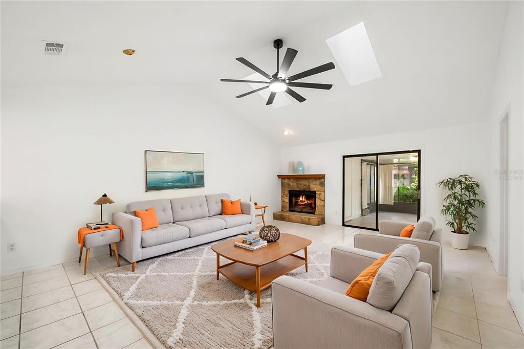 A living room features a stone fireplace, vaulted ceiling, ceiling fan, and light-colored tile flooring — 3723 NW 55TH PLACE, GAINESVILLE, FL