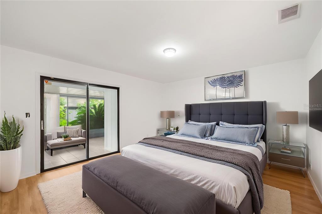 A bedroom features a gray upholstered bed, light wood floors, and sliding doors to a patio — 3723 NW 55TH PLACE, GAINESVILLE, FL
