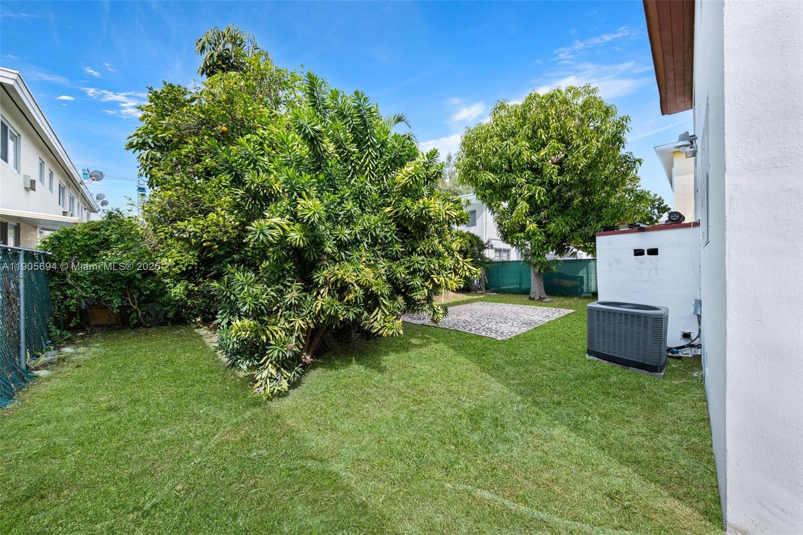 A grassy backyard features a large bush, a paved patio area, and an air conditioning unit — 7712 Byron Ave # 2, Miami Beach FL 33141, MIAMI BEACH, FL