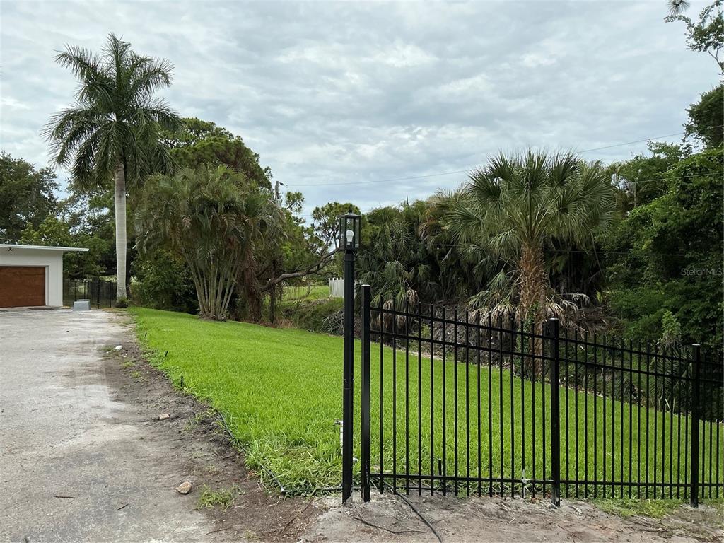 A black metal fence borders a grassy yard with palm trees and a paved driveway — 502 MAGELLAN DRIVE, SARASOTA, FL