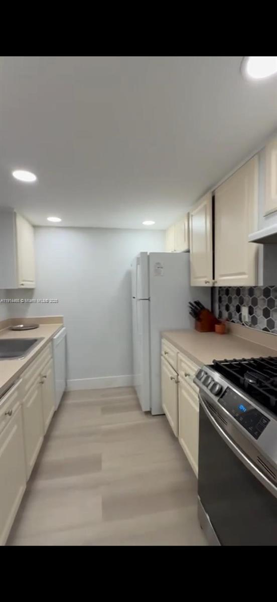 A galley-style kitchen features light-colored cabinetry, stainless steel appliances, and a hexagonal tile backsplash — 17901 NW 68 Ave # 205, Hialeah FL 33015, HIALEAH, FL
