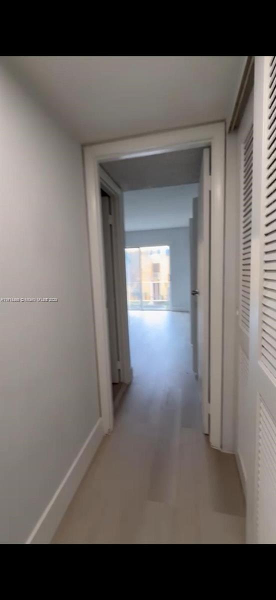 A hallway with light-colored flooring leads toward a bright room with a sliding glass door — 17901 NW 68 Ave # 205, Hialeah FL 33015, HIALEAH, FL