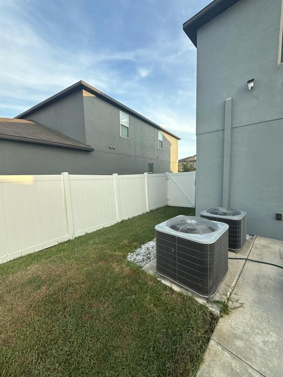 Two air conditioning units sit on a concrete pad next to a white vinyl fence — 10364 ALDER GREEN DRIVE, RIVERVIEW, FL