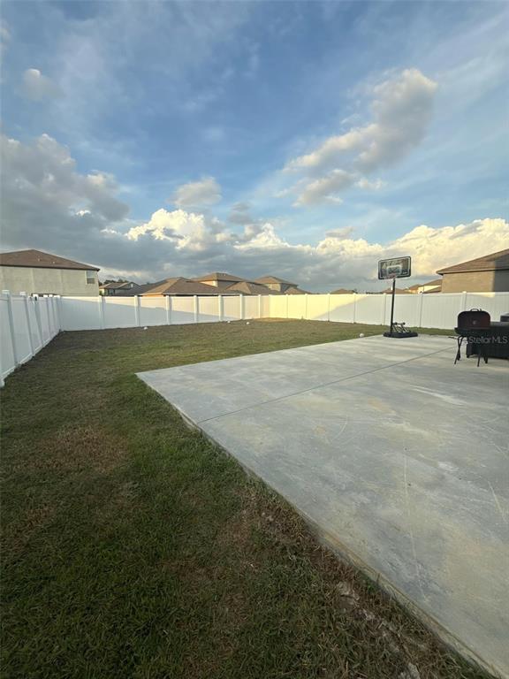 A backyard features a concrete patio, a basketball hoop, and a white vinyl privacy fence — 10364 ALDER GREEN DRIVE, RIVERVIEW, FL
