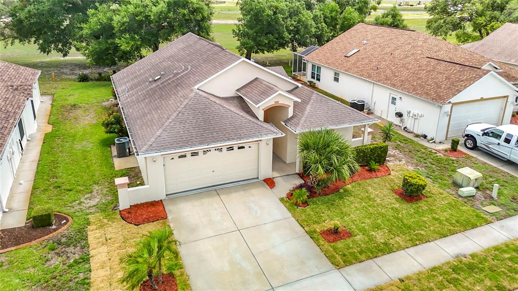 An aerial view shows a single-story house with a tan exterior, shingled roof, and driveway — 13203 GOLF RIDGE PLACE, HUDSON, FL
