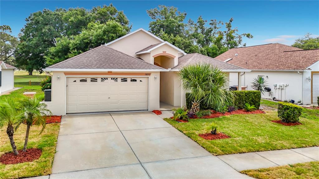 A single-story suburban house with a two-car garage, tan stucco exterior, and a concrete driveway — 13203 GOLF RIDGE PLACE, HUDSON, FL