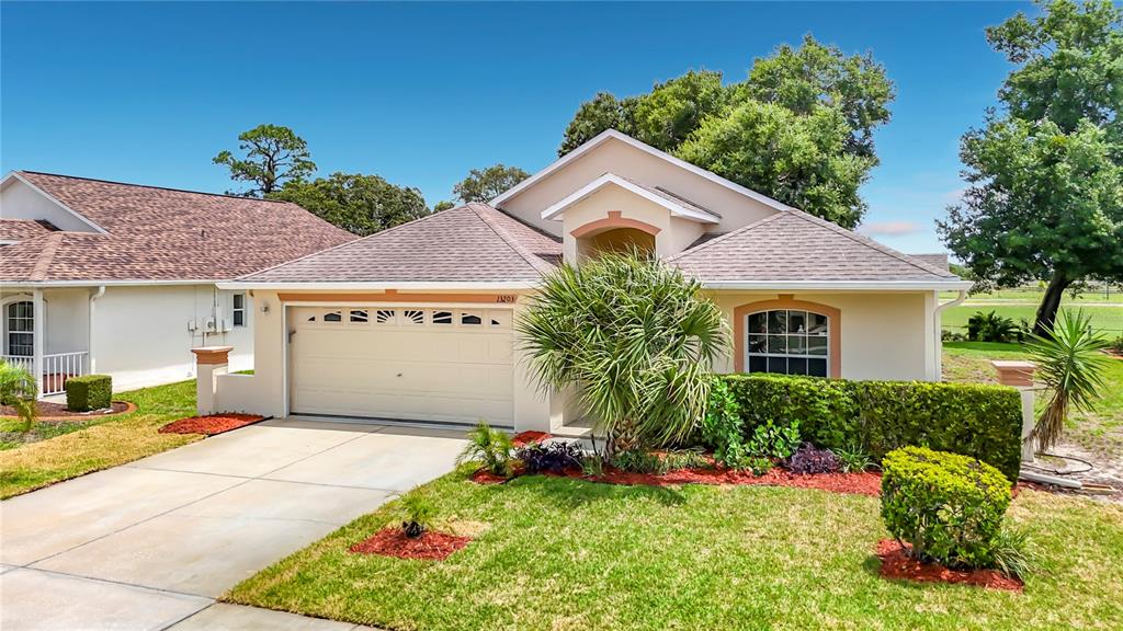 A single-story house with a beige exterior, a two-car garage, and a landscaped front yard — 13203 GOLF RIDGE PLACE, HUDSON, FL