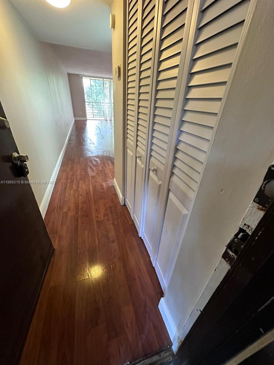 A hallway with wood-look flooring leads toward a window with vertical blinds — 3390 Foxcroft Rd # C212, Miramar FL 33025, MIRAMAR, FL