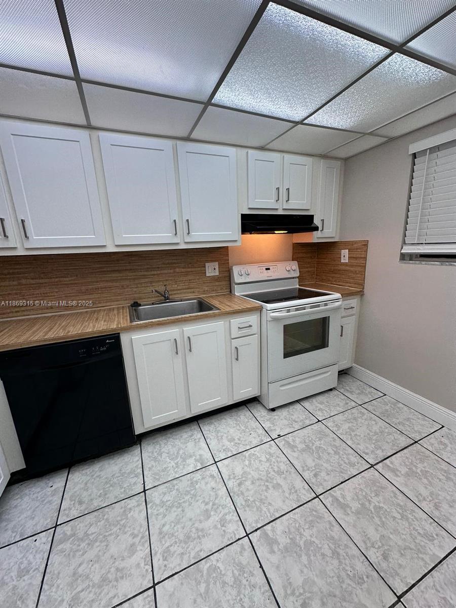 A kitchen features white cabinets, a black dishwasher, a white stove, and light-colored tile flooring — 3390 Foxcroft Rd # C212, Miramar FL 33025, MIRAMAR, FL