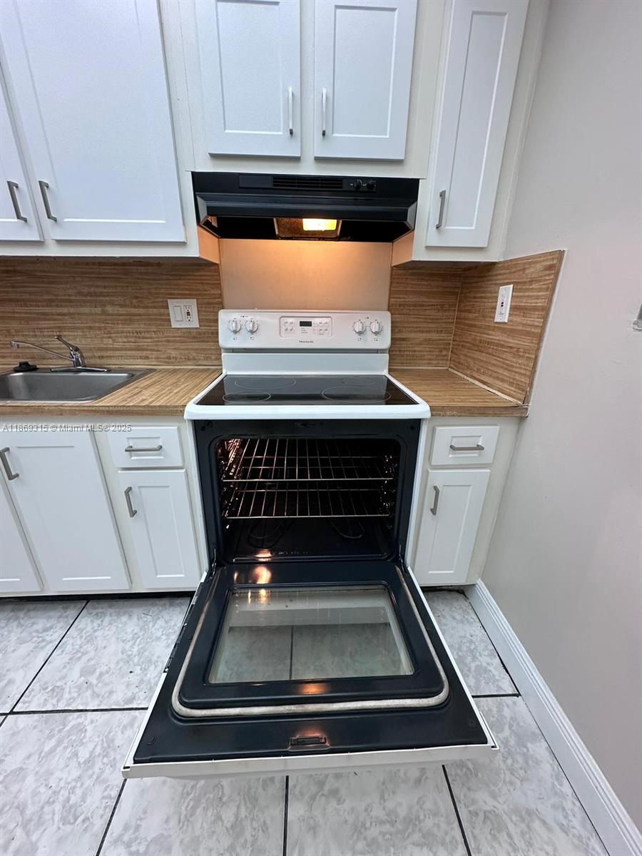 A kitchen features white cabinets, a wood-look countertop, and a white electric range — 3390 Foxcroft Rd # C212, Miramar FL 33025, MIRAMAR, FL