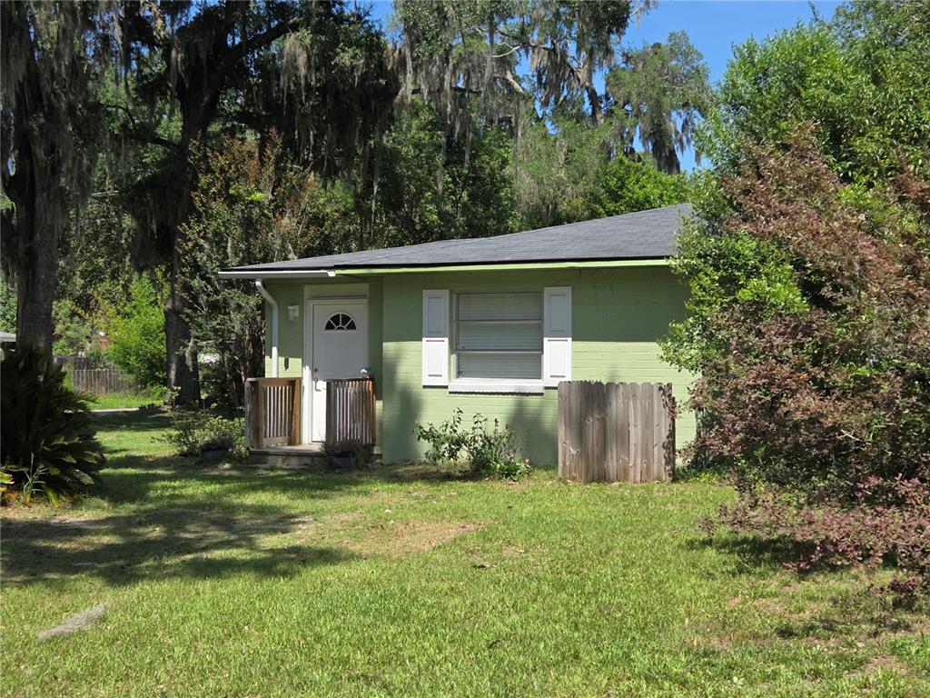 A small, light green house with white shutters and a wooden porch sits on grass — 725 NW 33RD AVENUE, GAINESVILLE, FL