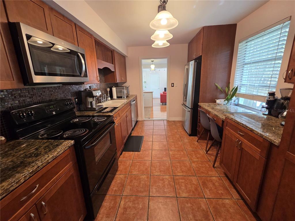 A galley kitchen features wood cabinets, granite countertops, stainless steel appliances, and tile flooring — 725 NW 33RD AVENUE, GAINESVILLE, FL