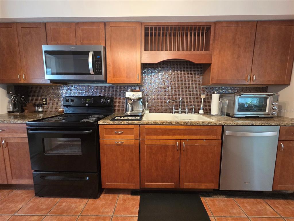 A kitchen features wood cabinets, a black stove, a stainless steel dishwasher, and tiled backsplash — 725 NW 33RD AVENUE, GAINESVILLE, FL