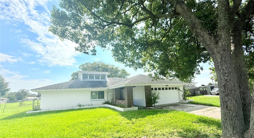 A white, single-story house with a brick accent wall sits under a large tree — 140 FAIRWAY TEN DRIVE, CASSELBERRY, FL
