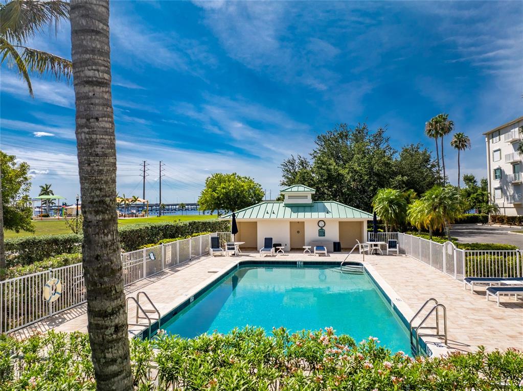 An outdoor swimming pool with a small clubhouse building and palm trees under a blue sky — 200 HARBOR WALK DRIVE UNIT 233, PUNTA GORDA, FL