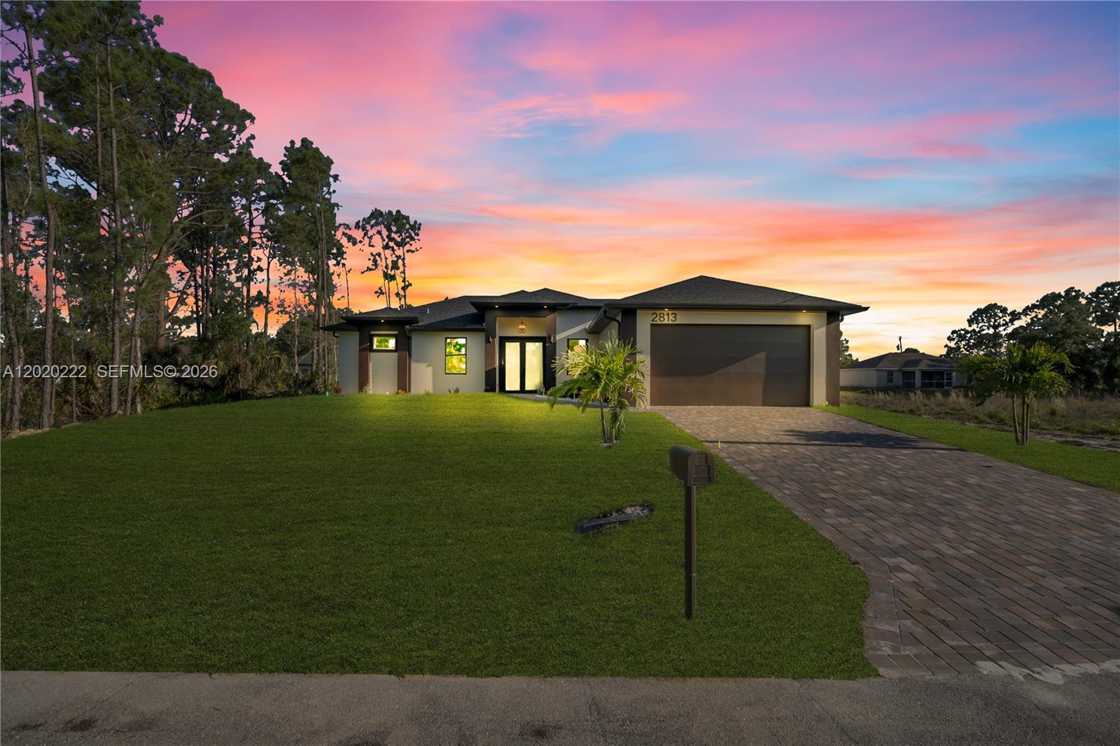 A modern single-story house with a paved driveway and a vibrant sunset sky — 2813 40th St W, Lehigh Acres FL 33971, LEHIGH ACRES, FL