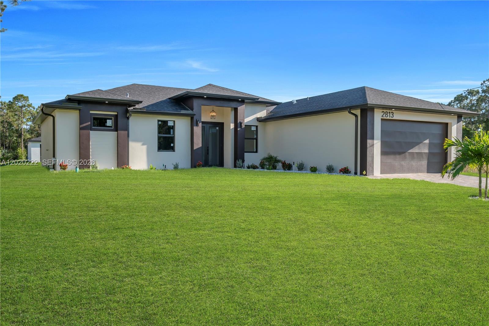 A modern single-story house features a dark-trimmed entryway, a two-car garage, and a large lawn — 2813 40th St W, Lehigh Acres FL 33971, LEHIGH ACRES, FL