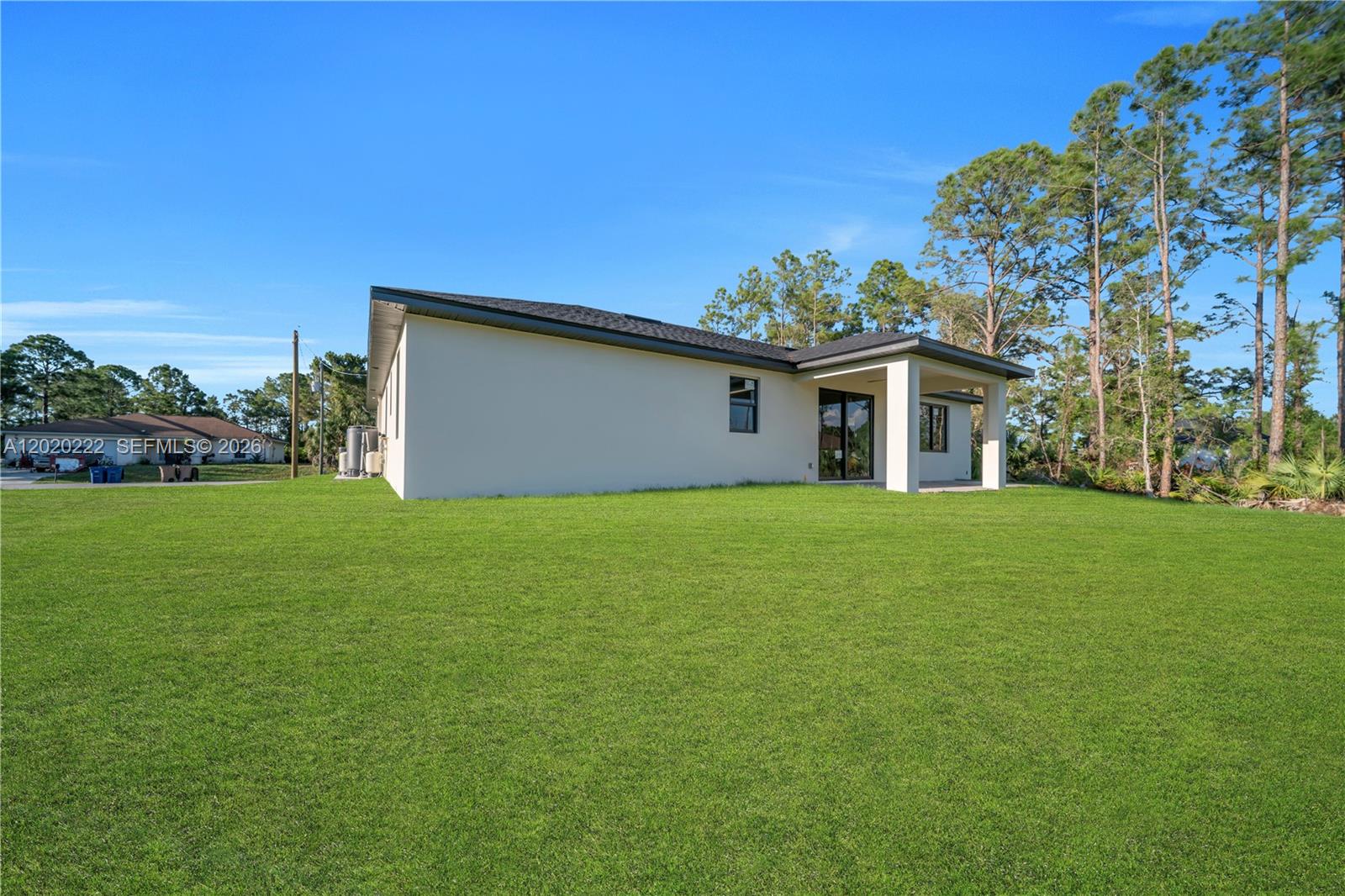 The exterior of a single-story house features a large grassy yard and a covered patio — 2813 40th St W, Lehigh Acres FL 33971, LEHIGH ACRES, FL