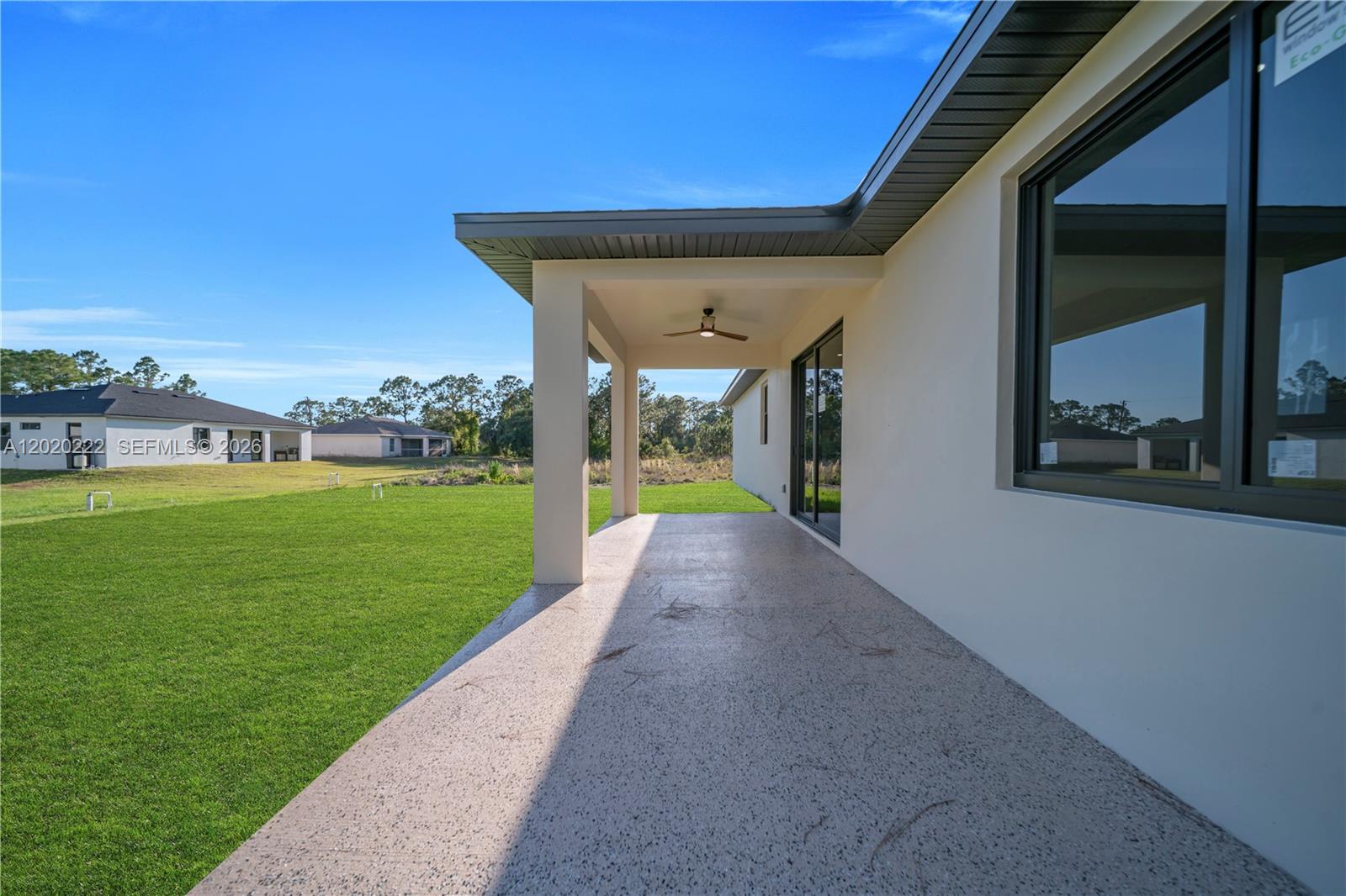 A covered concrete patio overlooks a large grassy backyard under a clear blue sky — 2813 40th St W, Lehigh Acres FL 33971, LEHIGH ACRES, FL