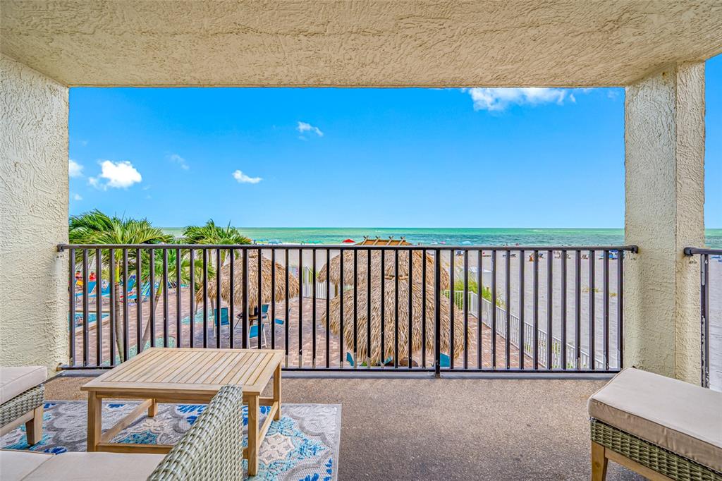 A balcony with outdoor furniture overlooks a beach, palm trees, and the ocean — 12924 GULF BOULEVARD UNIT 105, MADEIRA BEACH, FL