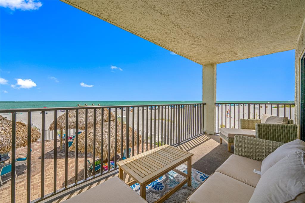 A balcony with outdoor furniture overlooks a sandy beach and the ocean — 12924 GULF BOULEVARD UNIT 105, MADEIRA BEACH, FL