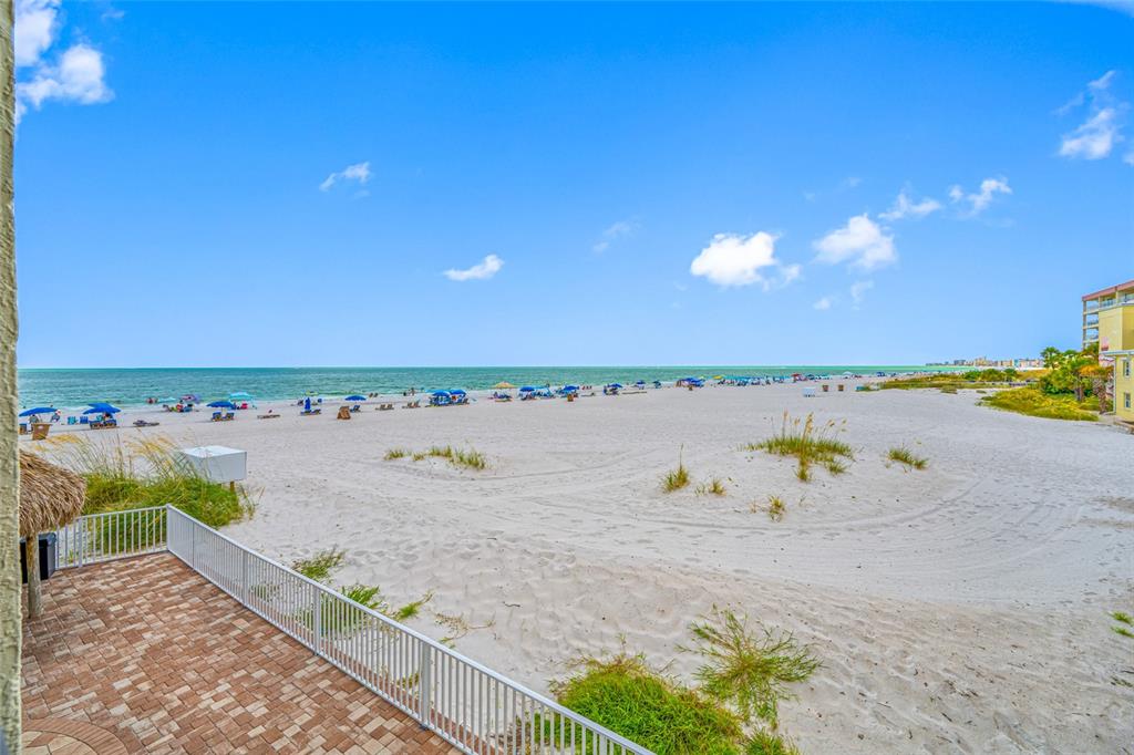 An elevated view of a sandy beach with umbrellas and the ocean from a patio — 12924 GULF BOULEVARD UNIT 105, MADEIRA BEACH, FL