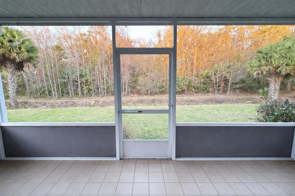 A tiled screened-in porch overlooks a grassy backyard with trees and palms — 2401 SW 20TH COURT, OCALA, FL
