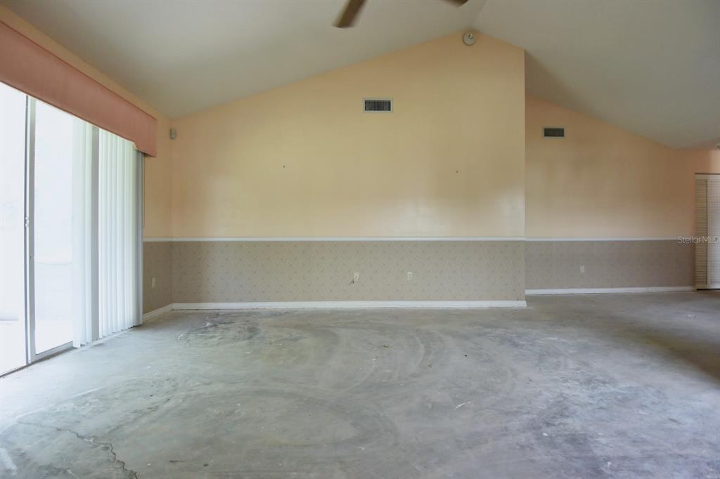 An empty room with vaulted ceilings, beige walls, wallpaper wainscoting, and a concrete floor — 2401 SW 20TH COURT, OCALA, FL