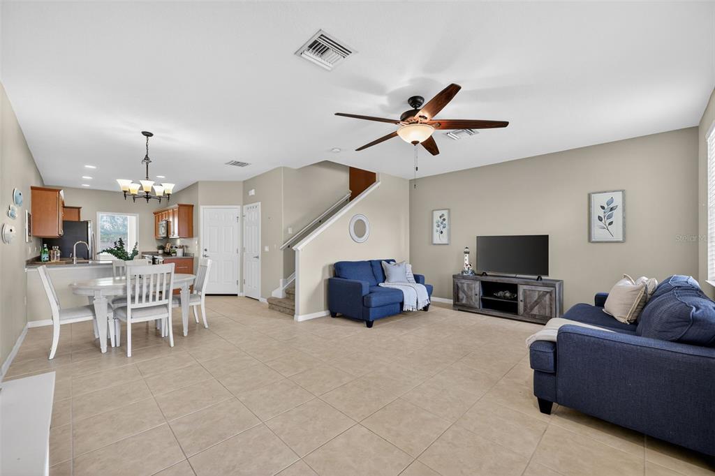 An open-concept living and dining area features tile flooring, blue sofas, and a ceiling fan — 3736 82ND AVENUE CIRCLE E UNIT 105, SARASOTA, FL