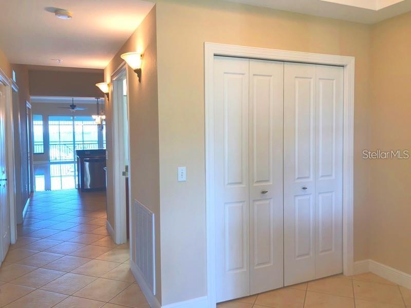 A hallway with tile flooring leads to a kitchen area past a white bi-fold closet — 5114 MELBOURNE STREET UNIT 1301, PORT CHARLOTTE, FL