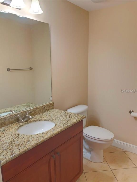 A bathroom featuring a granite vanity, wood cabinets, a mirror, and a white toilet — 5114 MELBOURNE STREET UNIT 1301, PORT CHARLOTTE, FL