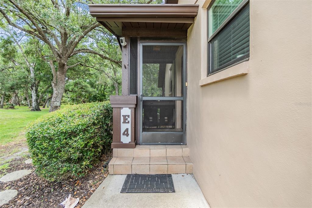 A tan exterior wall features a screened front door with a unit number E4 sign — 1400 TARPON WOODS BOULEVARD UNIT E4, PALM HARBOR, FL