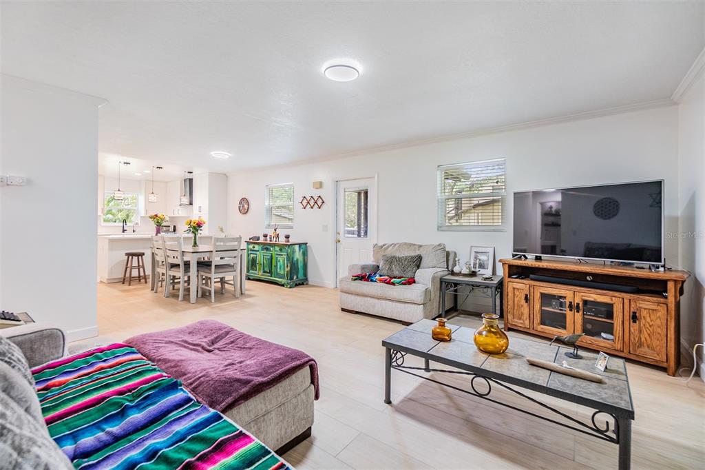 A bright living room features light wood flooring, a television console, and an open kitchen — 1400 TARPON WOODS BOULEVARD UNIT E4, PALM HARBOR, FL
