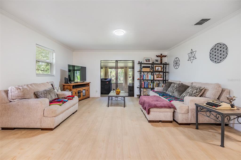 A living room features light wood flooring, two beige sofas, a bookshelf, and a television — 1400 TARPON WOODS BOULEVARD UNIT E4, PALM HARBOR, FL