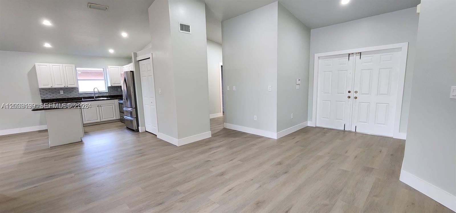 An open-concept room features light wood-look flooring, white double doors, and an adjacent kitchen area — 14817 SW 180th St, Miami FL 33187, MIAMI, FL