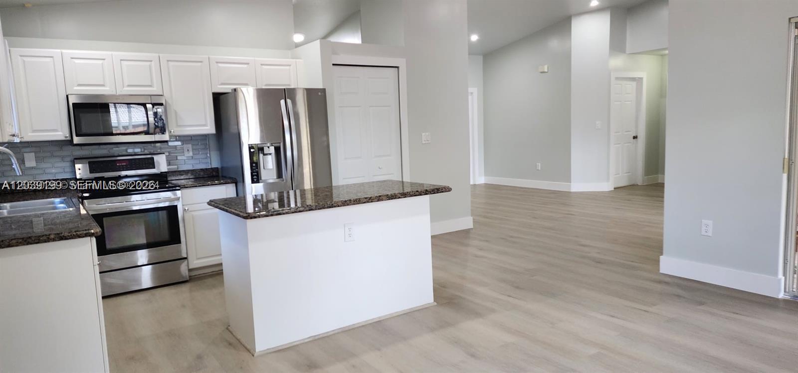 A kitchen with white cabinets, stainless steel appliances, and a granite-topped island opens to a living area — 14817 SW 180th St, Miami FL 33187, MIAMI, FL