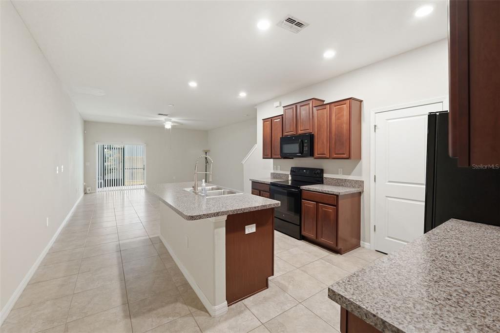 A kitchen with dark wood cabinets, granite countertops, and an island overlooks an open living area — 10407 LAKE MONTAUK DRIVE, RIVERVIEW, FL